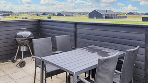 An outdoor patio with a table and chairs, a grill, and a view of a residential area.