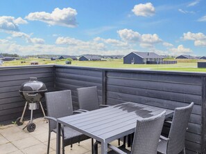 An outdoor patio with a table and chairs, a grill, and a view of a residential area. - 5 Star Holiday Home in Lokken (Lokken)