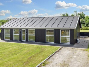 A modern building with a sloped roof, large windows, and a paved entrance area.