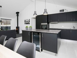 A modern kitchen with dark cabinetry, a central island, and pendant lighting. - 5 Star Holiday Home in Lokken (Lokken)