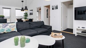 A modern living room with a grey sofa, a white coffee table, and a television on a white stand.