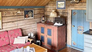 L’intérieur d’un chalet accueillant, avec un plafond en bois, un buffet rouge agrémenté de touches de bleu, un canapé rose et une petite table recouverte d’une nappe à carreaux.
