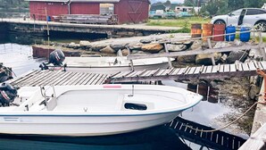 Un quai avec un bateau blanc, une grange rouge et une voiture au loin.