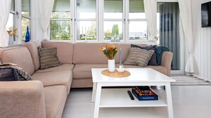 Una sala de estar moderna con un sofá color beige, una mesa de centro blanca y un televisor en la pared.