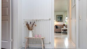 Un pasillo con baldosas azules y blancas estampadas, una puerta blanca y una pequeña mesa de madera con un jarrón de flores secas y velas.