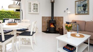 Una sala de estar acogedora con interior blanco, una chimenea de piedra, una zona de comedor con mobiliario blanco y un cuadro en la pared.