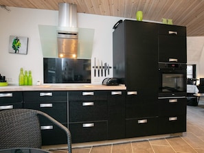 A modern kitchen with a black refrigerator, stainless steel appliances, and a wooden ceiling.