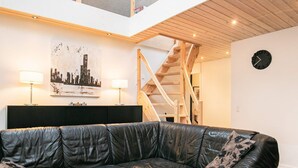Ett modernt vardagsrum med en svart lädersoffa, ett runt soffbord och en trappa som leder upp till en övre våning.