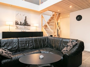 A modern living room with a black leather sectional sofa, a round coffee table, and a staircase leading to an upper level. - 4 Star Holiday Home in Laeso (Læsø)