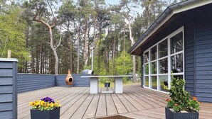 A wooden deck with a built-in grill and seating area, surrounded by a dark blue house with large windows. - 4 Star Holiday Home in Laeso (Læsø)