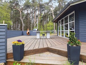 A wooden deck with a built-in grill and seating area, surrounded by a dark blue house with large windows. - 4 Star Holiday Home in Laeso (Læsø)
