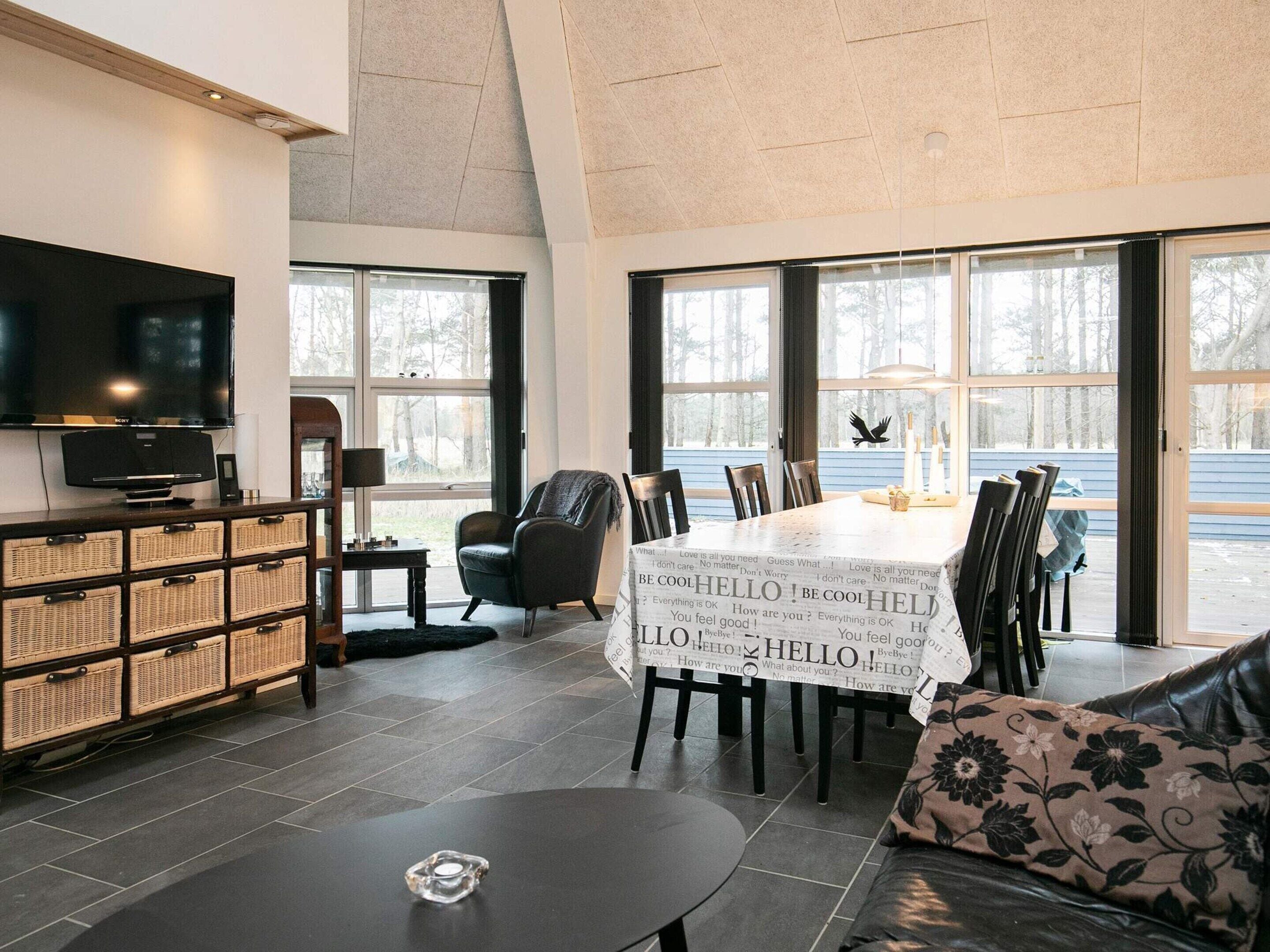 A spacious living area with a large TV, wicker storage, a dining table with a 'HELLO' banner, and a view of the outdoors.