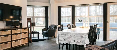A spacious living area with a large TV, wicker storage, a dining table with a 'HELLO' banner, and a view of the outdoors.