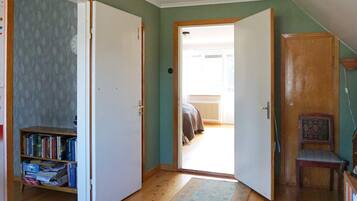 A room with a wooden floor, a bookshelf, a door leading to a balcony, and a chair.