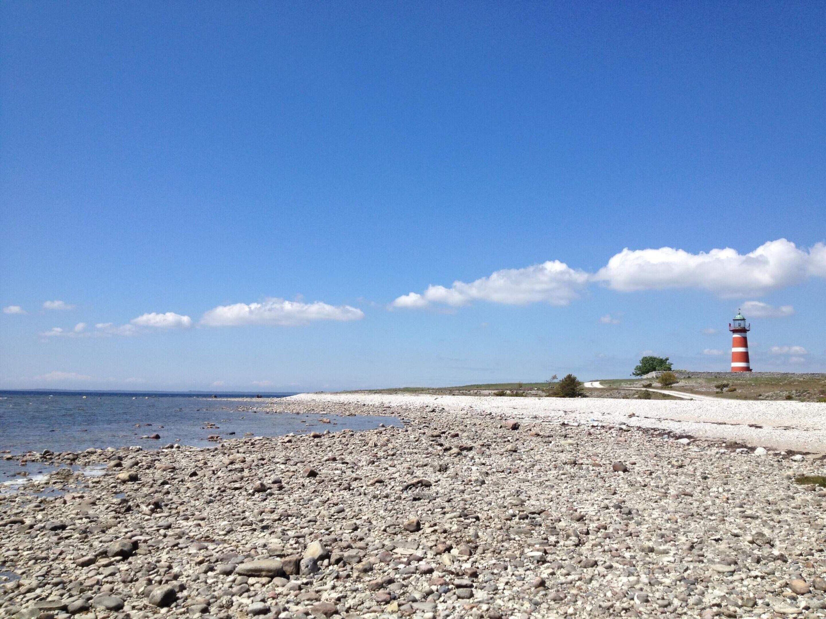 A pebbled beach with a lighthouse in the distance.