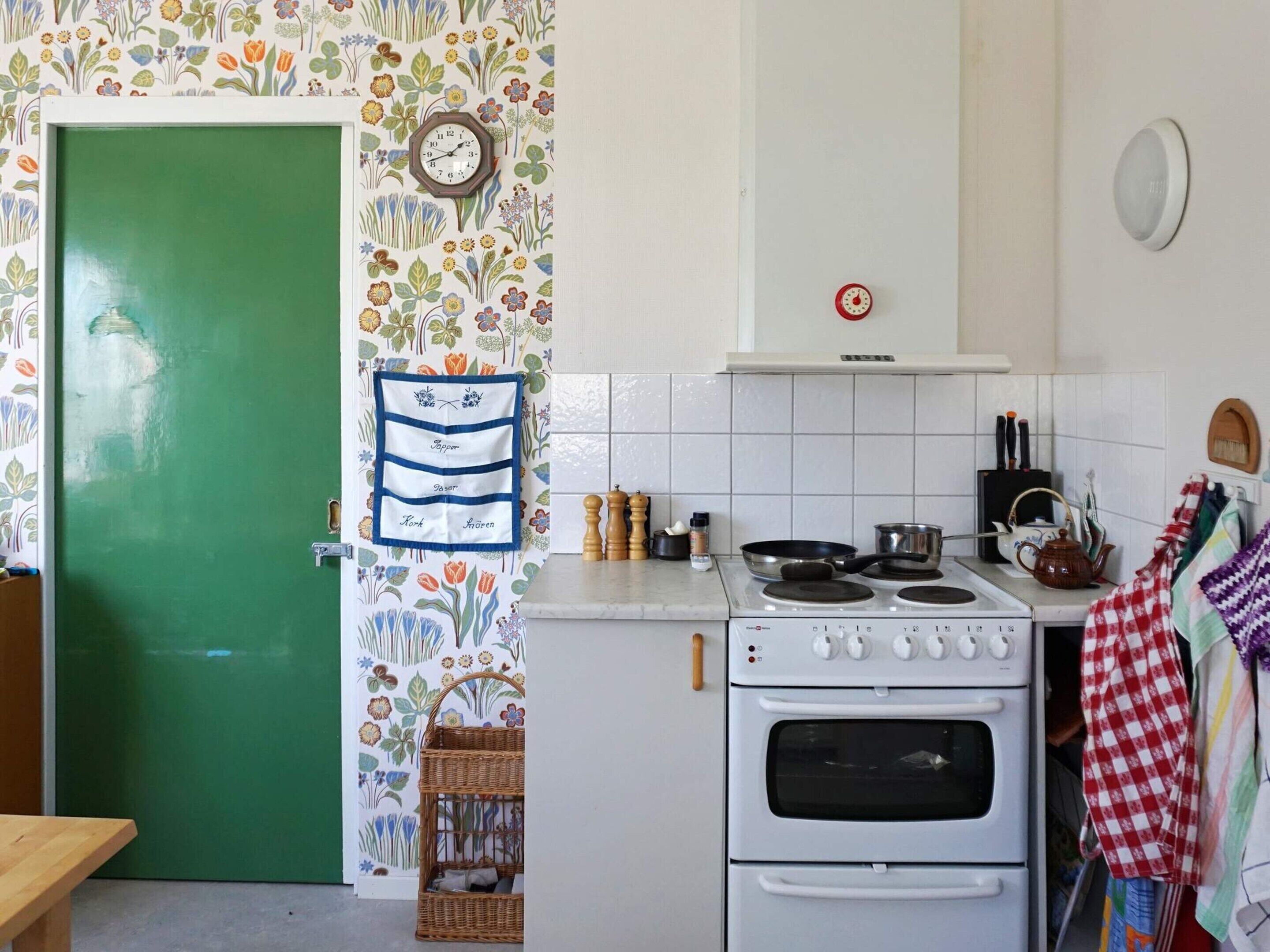 A kitchen with a green door, a wall clock, a stove, and a hanging kitchen towel.