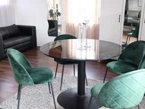 A round glass table with four chairs, a black sofa, and a white rug in a room with wooden flooring. - 4 Star Holiday Home in Munka-ljungby (Munka-Ljungby)