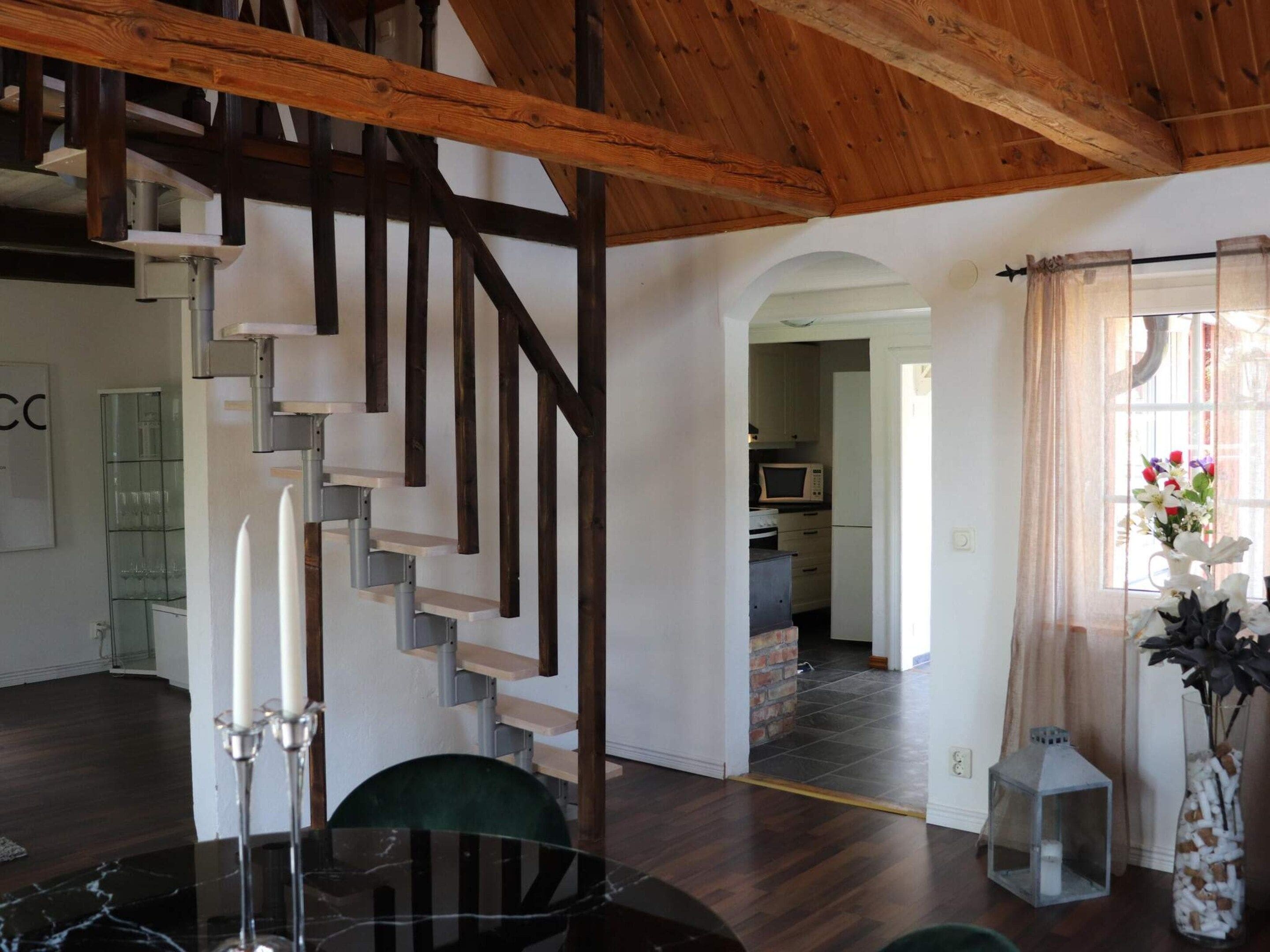 A modern interior with a spiral staircase, a dining area, and a kitchen visible through an open doorway.