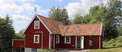 A red wooden house with a tiled roof, a chimney, and a small porch.