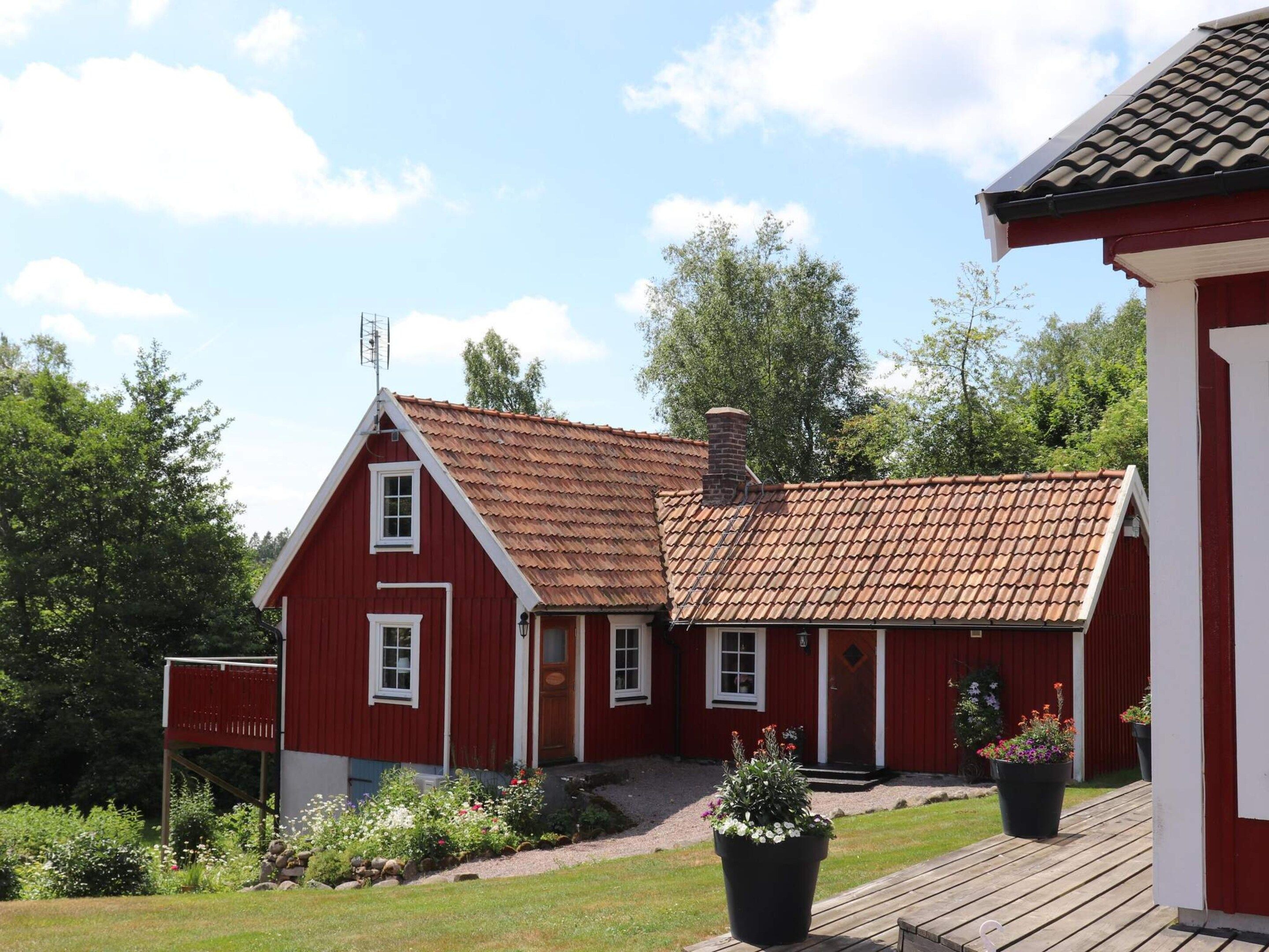 A red building with a sloped roof, a chimney, and a small porch with potted plants.
