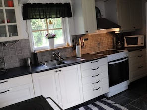 A modern kitchen with white cabinets, a black countertop, a sink, a microwave, and a stove. - 4 Star Holiday Home in Munka-ljungby (Munka-Ljungby)