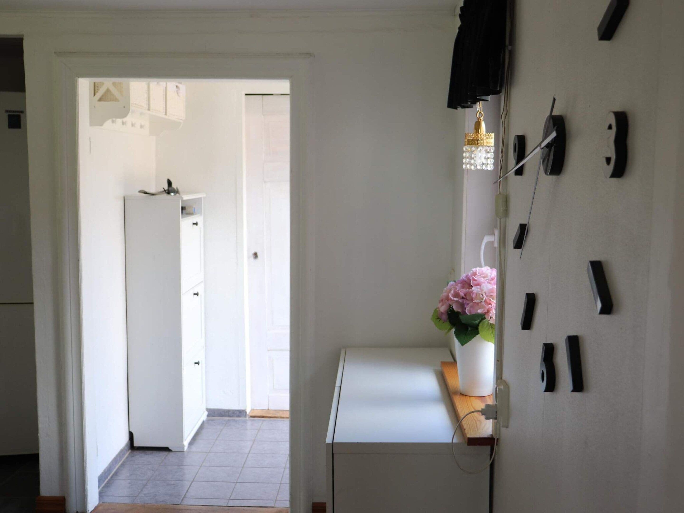 A hallway with a white door leading to a kitchen, a white cabinet, and a wall-mounted light fixture.