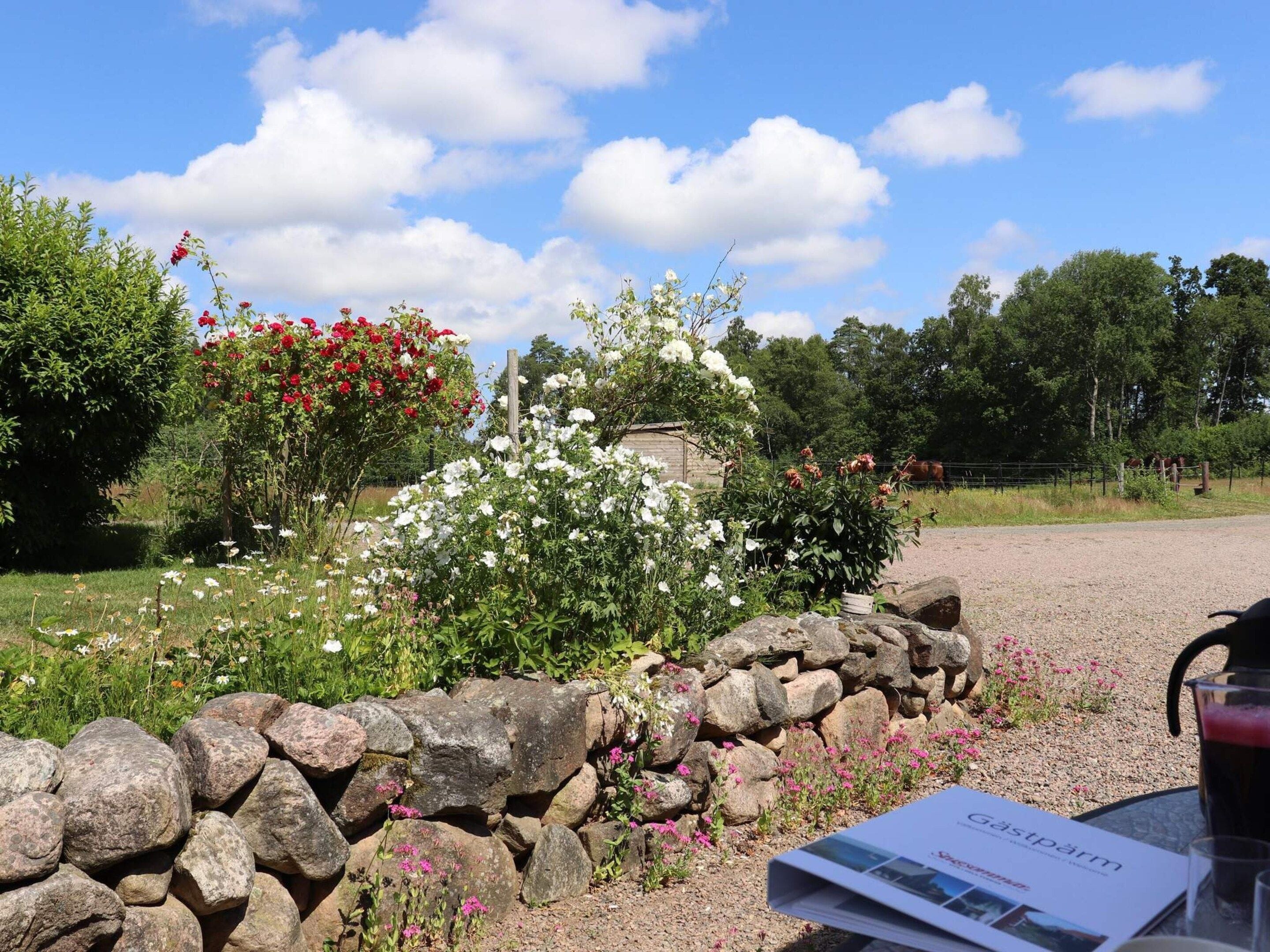 A garden with a stone wall, flowers, and a table with a menu and a drink.