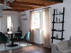 A dining area with a round table, two chairs, a wooden ceiling, a window with curtains, and a black shelf with decorative items. - 4 Star Holiday Home in Munka-ljungby (Munka-Ljungby)