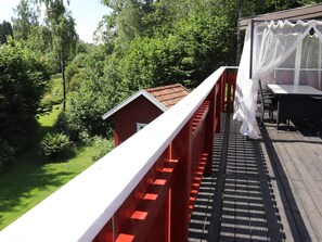 A red wooden deck with a white railing, a table, and a covered area with a white curtain. - 4 Star Holiday Home in Munka-ljungby (Munka-Ljungby)