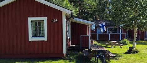 A red cabin with a window and the number B23, a picnic table, and a flag.