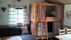 Una stanza accogliente con un divano, un tavolo, un letto a castello con tende decorate, una scala e una sveglia a muro.