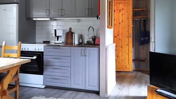 Una cucina compatta con mobili grigi, un fornello, una macchina per il caffè e una porta in legno che dà su un bagno.