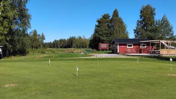A golf course with a red building, a picnic area, and a clear sky.