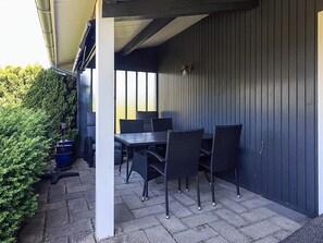 An outdoor patio area with a table and chairs, a dark wall, and a hedge. - 4 Person Holiday Home in Faxe Ladeplads (Faxe Ladeplads)