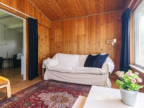 A cozy room with a wooden ceiling, a white sofa with pillows, a patterned rug, and a potted plant with flowers. - 4 Person Holiday Home in Faxe Ladeplads (Faxe Ladeplads)