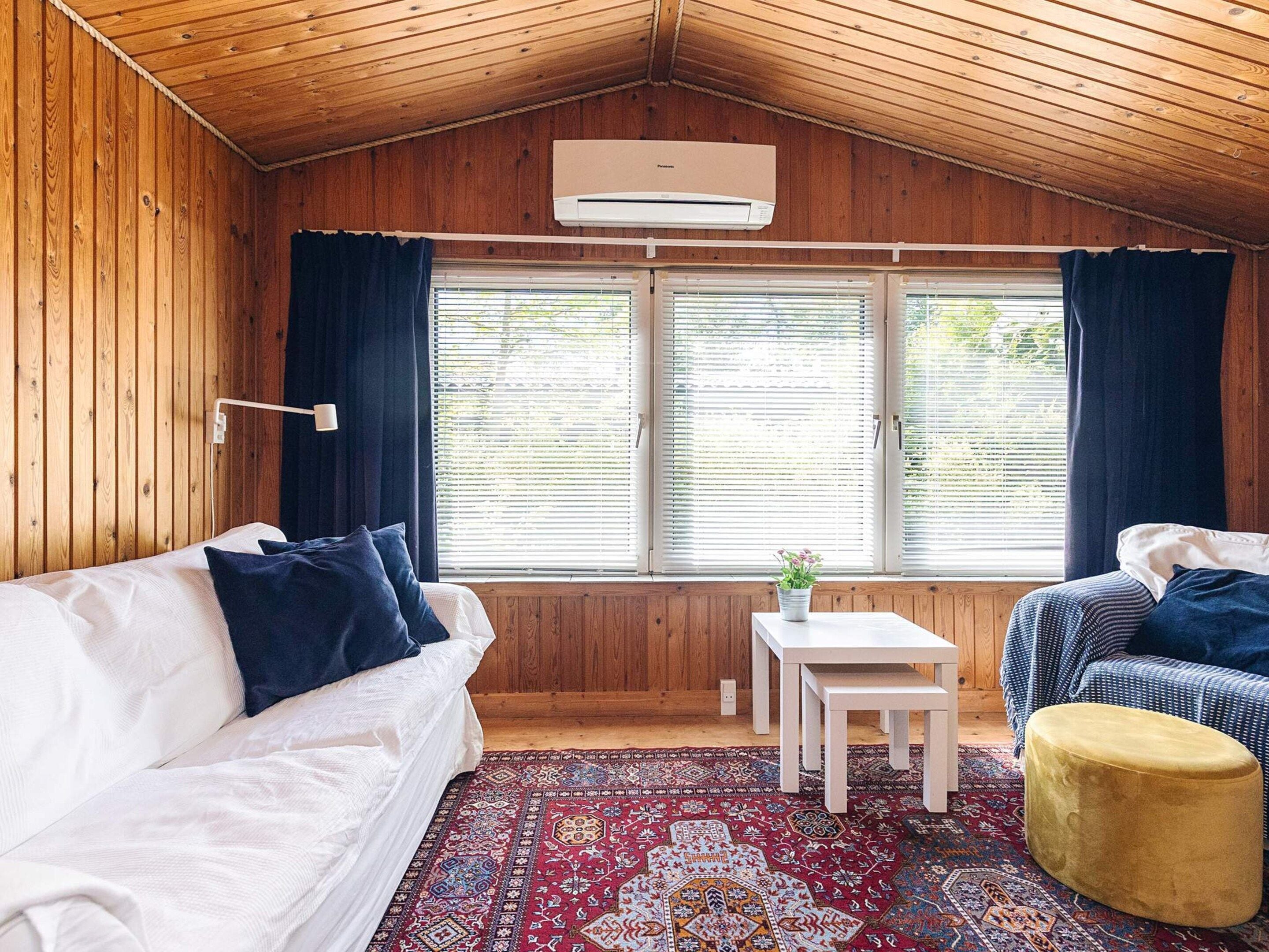 A cozy room with a wooden ceiling, a white sofa, a small table with a plant, and a patterned rug.
