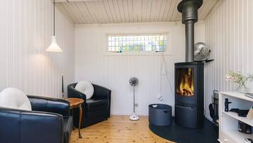 Ett mysigt vardagsrum med en öppen spis, en svart lädersoffa, en vit fåtölj och ett trägolv.