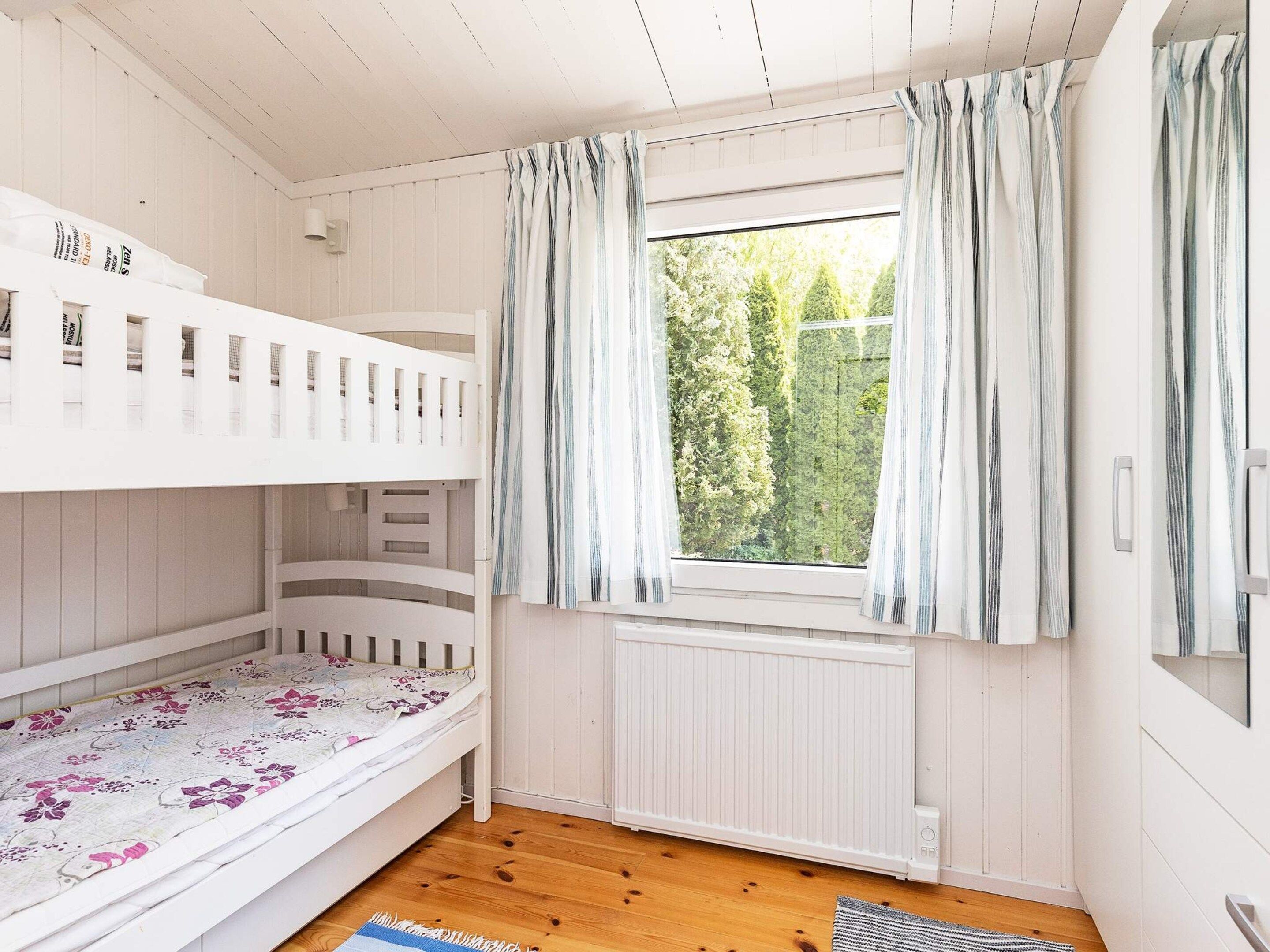 Et værelse med køjesenge, et vindue med gardiner, en radiator og et trægulv.