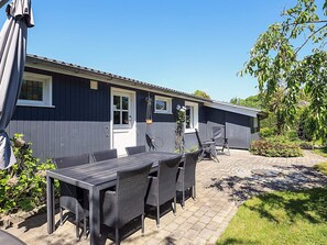A patio area with a table and chairs, a hanging basket, and a small shed. - 4 Person Holiday Home in Faxe Ladeplads (Faxe Ladeplads)