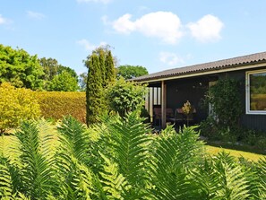 A house with a covered porch, surrounded by lush greenery and a well-maintained hedge. - 4 Person Holiday Home in Faxe Ladeplads (Faxe Ladeplads)