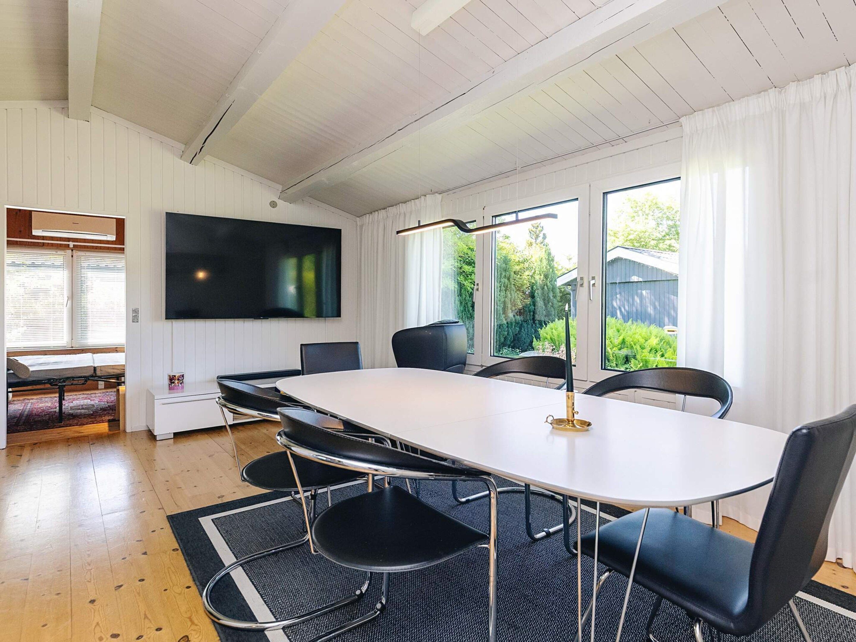 A modern dining area with a white table, black chairs, and a flat-screen TV mounted on the wall.