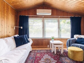 A cozy room with a wooden ceiling, a white sofa, a small table, and a yellow ottoman. - 4 Person Holiday Home in Faxe Ladeplads (Faxe Ladeplads)