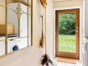 A laundry room with a washing machine, a door leading to a garden, and a mirror with a decorative frame.