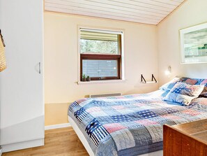 A bedroom with a bed, a window, a radiator, and a wall-mounted shelf.