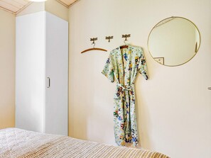 A bedroom with a bed, a wardrobe, a robe hanging on a hook, and a round mirror on the wall.