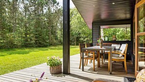 Una terraza de madera con mobiliario exterior, una mesa y sillas.