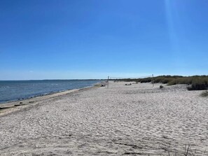 En strand med ett volleybollnät, sandig mark och en klar himmel.