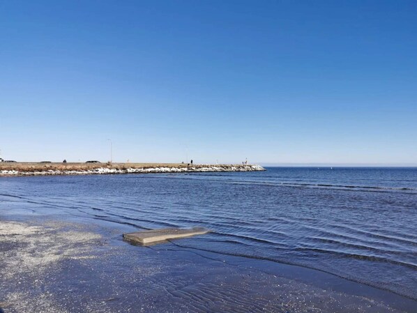 A coastal scene with a clear sky, calm sea, and a rocky breakwater.