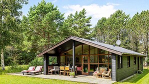 Una cabaña con terraza, mobiliario exterior y ventanas amplias.