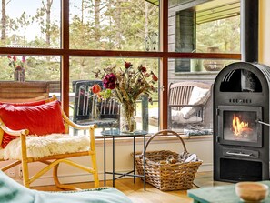 A cozy room with a large window, a wicker basket, a red chair, and a wood-burning stove.